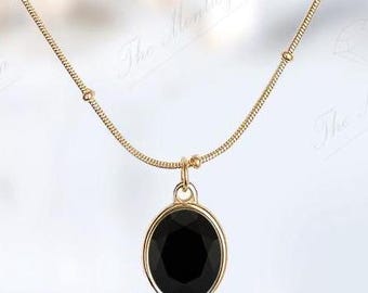 Pode incluir: Um colar de corrente de ouro com um pingente oval preto. O pingente tem uma pedra preta facetada.
