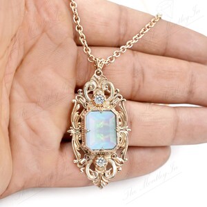 May include: A gold necklace with a large, ornate pendant featuring a white opal gemstone surrounded by smaller clear stones.