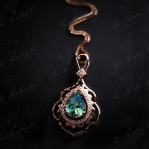 Puede incluir: Un collar con colgante de oro rosa con una piedra preciosa azul-verdosa en forma de l&aacute;grima. El colgante est&aacute; adornado con peque&ntilde;as piedras transparentes y filigrana de oro rosa. La cadena tambi&eacute;n es de oro rosa, sobre un fondo negro.