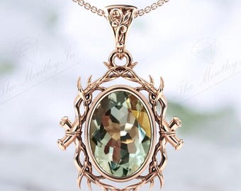 Può includere: Una collana con un ciondolo in oro rosa ornato con una grande pietra preziosa ovale verde incastonata in una cornice dettagliata e decorata. La cornice è in metallo ritorto con un design spinoso.