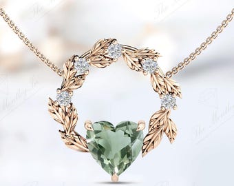 Può includere: Una delicata collana d'oro con un ciondolo a forma di cuore in pietra preziosa verde circondato da una ghirlanda di foglie e piccoli diamanti.