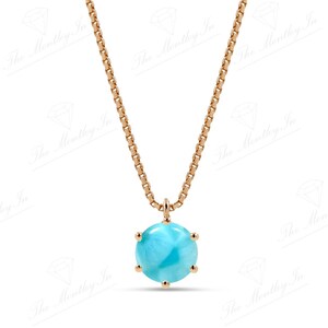 Op de afbeelding: Een gouden ketting met een blauwe edelsteen hanger. De hanger is rond en heeft een facetgeslepen ontwerp.