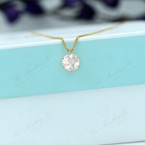 Pu&ograve; includere: Una collana d'oro con un pendente di pietra preziosa rosa chiaro, appoggiata su una scatola azzurra e bianca. Il pendente ha una forma esagonale. La collana &egrave; delicata ed elegante.