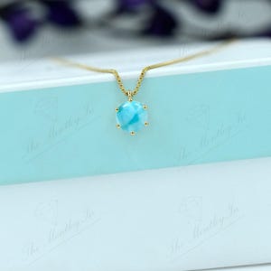 Op de afbeelding: Een gouden ketting met een blauwe en witte edelsteen hanger. De hanger is rond en heeft een gouden zetting.