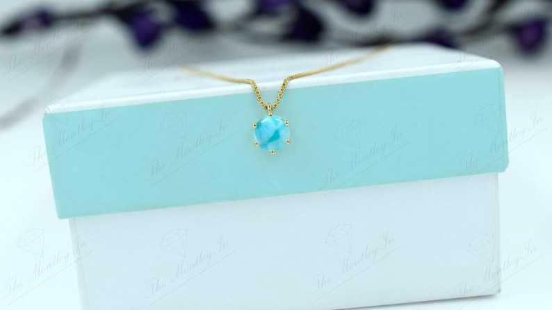 Op de afbeelding: Een gouden ketting met een blauwe en witte edelsteen hanger. De hanger is rond en heeft een gouden zetting.