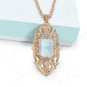 May include: A gold necklace with a large, ornate pendant featuring a rectangular iridescent stone surrounded by smaller clear stones.