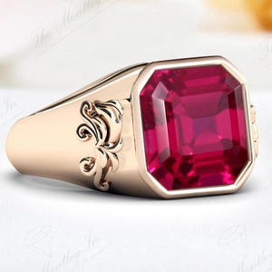 May include: A gold ring with a large, square-shaped ruby gemstone. The ring has a decorative design on the side.