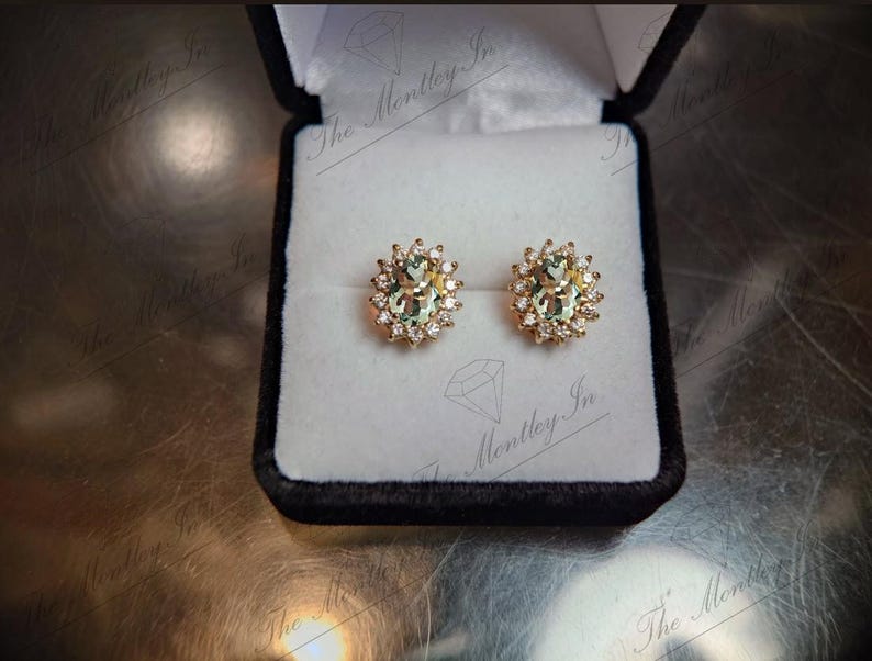 May include: A pair of gold earrings with oval-shaped green gemstones surrounded by smaller clear gemstones.