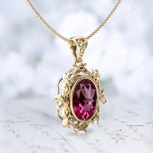 May include: A gold pendant necklace with a pink oval gemstone set in a delicate floral design.