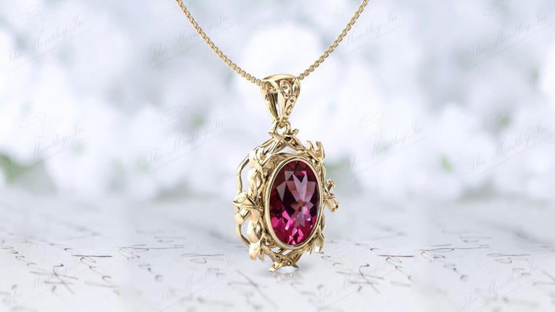 May include: A gold pendant necklace with a pink oval gemstone set in a delicate floral design.