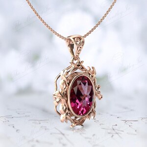 May include: A rose gold pendant necklace with a large oval-shaped pink gemstone set in a delicate, ornate frame. The frame features intricate floral designs.