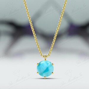 Op de afbeelding: Een gouden ketting met een ronde blauwe edelsteen hanger.