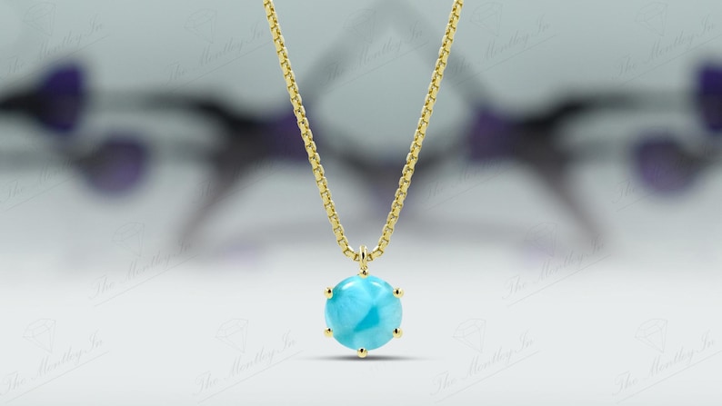 Op de afbeelding: Een gouden ketting met een ronde blauwe edelsteen hanger.