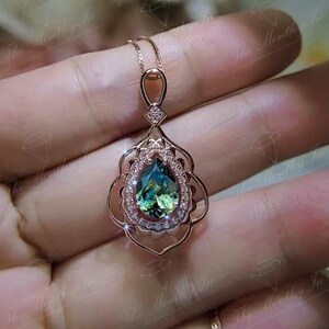 Puede incluir: Collar con colgante de oro rosa con una piedra preciosa verde azulada en forma de pera, rodeada por un halo de peque&ntilde;as piedras claras. El colgante tiene un dise&ntilde;o calado ornamentado y una cadena delicada.