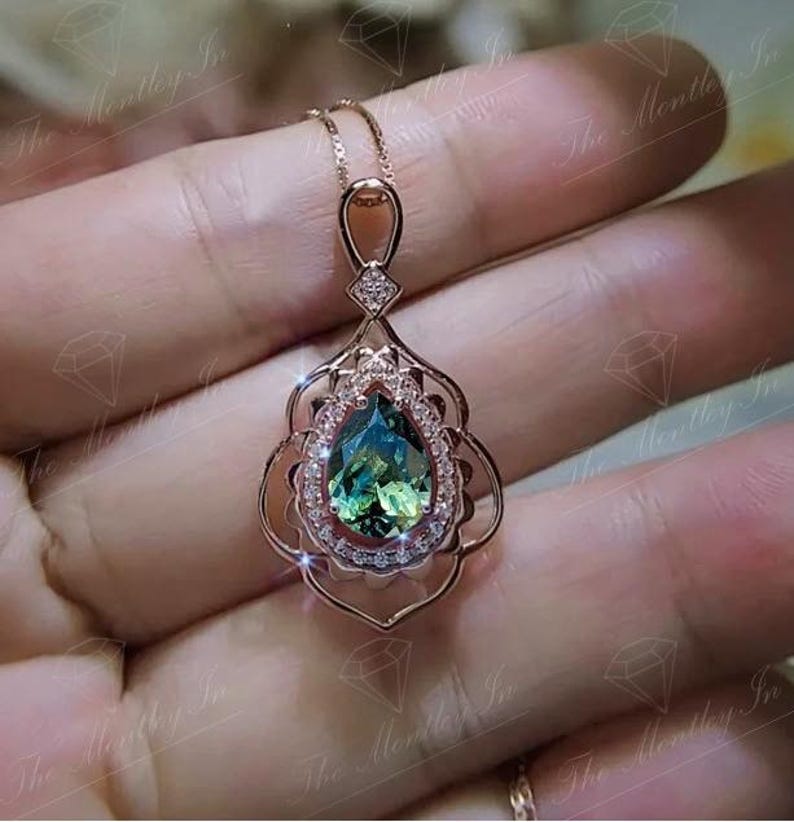 Puede incluir: Collar con colgante de oro rosa con una piedra preciosa verde azulada en forma de pera, rodeada por un halo de peque&ntilde;as piedras claras. El colgante tiene un dise&ntilde;o calado ornamentado y una cadena delicada.