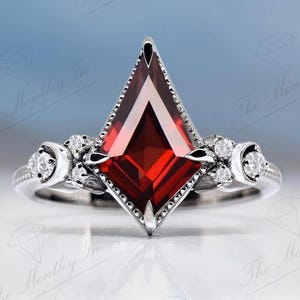 Peut inclure: Une bague en argent avec une grande pierre précieuse rouge en forme de cerf-volant et de plus petites pierres précieuses claires sur la bande.
