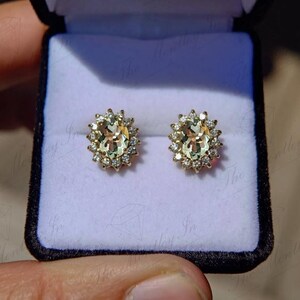 May include: A pair of gold earrings with oval-shaped green gemstones surrounded by a halo of smaller diamonds.