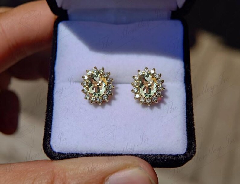 May include: A pair of gold earrings with oval-shaped green gemstones surrounded by a halo of smaller diamonds.