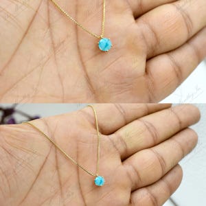 Op de afbeelding: Een gouden ketting met een klein, rond, lichtblauw edelsteen hanger.