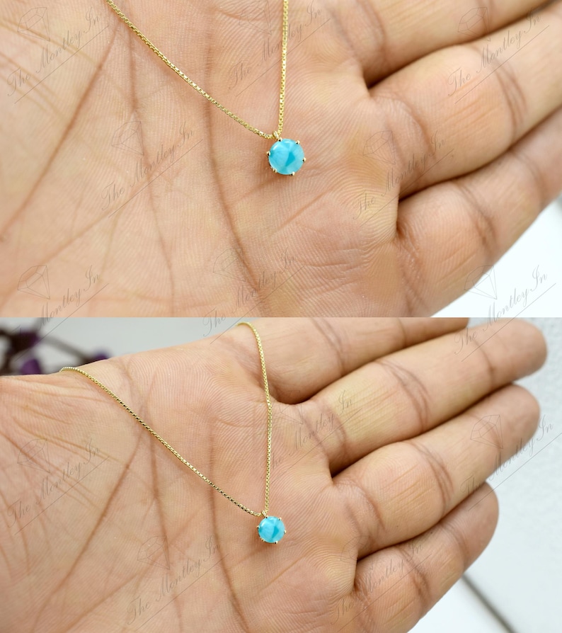 Op de afbeelding: Een gouden ketting met een klein, rond, lichtblauw edelsteen hanger.