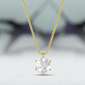 Pu&ograve; includere: Una collana color oro con un pendente di pietra preziosa trasparente e rotonda. Il pendente &egrave; incastonato in una montatura a sei punte e pende da una catena delicata. Lo sfondo &egrave; sfocato, con sfumature viola.