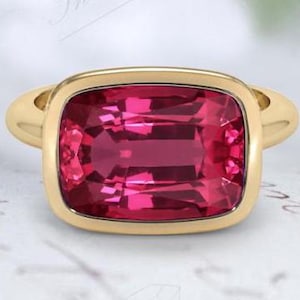 Puede incluir: Un anillo de oro con una gran piedra preciosa rosa brillante engastada en un bisel cuadrado.