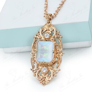 May include: A gold-tone necklace with a large, ornate pendant featuring a rectangular, iridescent white stone surrounded by smaller clear stones.