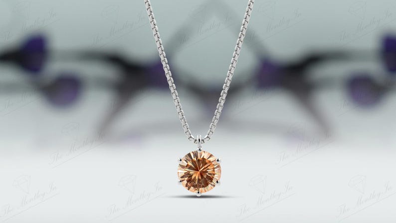 May include: A silver necklace with a round, light orange gemstone pendant. The pendant is the focal point, suspended from a delicate chain. The background is blurred, emphasizing the jewelry.