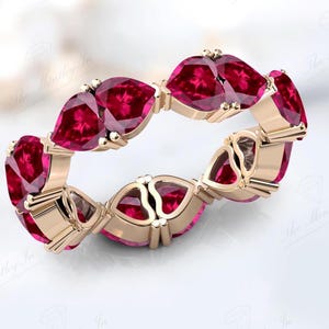 May include: A rose gold eternity band featuring a row of vibrant red pear-shaped gemstones.