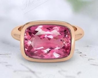 May include: A rose gold ring with a large, pink, cushion-cut gemstone.