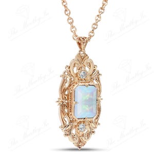 May include: A gold pendant necklace with a large, rectangular, iridescent opal gemstone set in a detailed, ornate, filigree frame. The frame is accented with two smaller, round, clear gemstones.