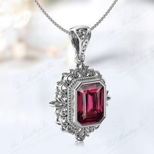 May include: A silver pendant necklace featuring an intricate filigree design and a large, rectangular, emerald-cut, pink gemstone.