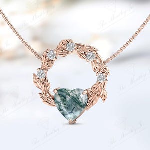 May include: A rose gold necklace with a heart-shaped green agate pendant surrounded by a wreath of leaves and small diamonds.