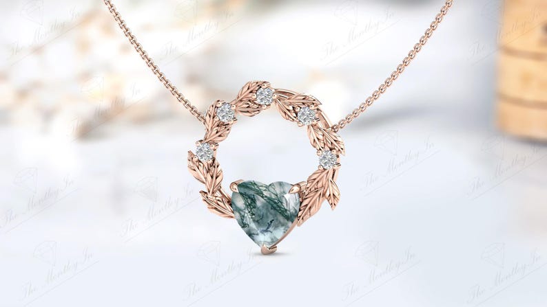 May include: A rose gold necklace with a heart-shaped green agate pendant surrounded by a wreath of leaves and small diamonds.