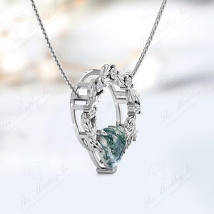 May include: A silver necklace with a pendant featuring a green and white stone surrounded by a silver wreath with small clear stones.
