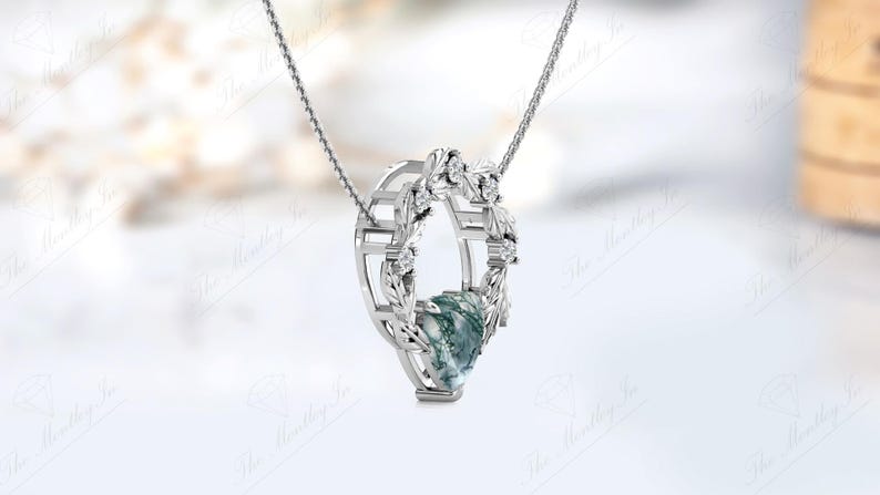 May include: A silver necklace with a pendant featuring a green and white stone surrounded by a silver wreath with small clear stones.