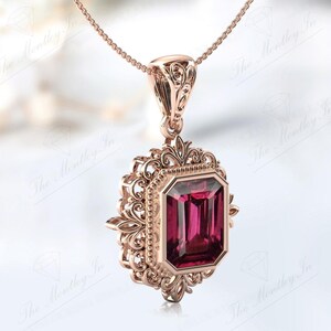 May include: A rose gold pendant necklace featuring an intricate filigree design and a large, rectangular, deep red gemstone.