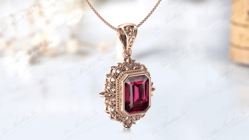 May include: A rose gold pendant necklace featuring an intricate filigree design and a large, rectangular, deep red gemstone.