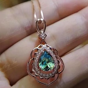 Puede incluir: Collar con colgante de oro rosa con una piedra preciosa en forma de pera, de color verde y azul. La piedra est&aacute; rodeada de peque&ntilde;os cristales transparentes y engastada en un marco calado decorativo. La cadena del collar es delicada.