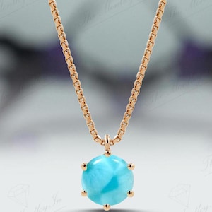 Op de afbeelding: Een delicate gouden ketting met een ronde blauwe edelsteen hanger. De hanger is gezet in een gouden bezel met vier klauwen.