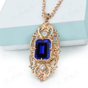 May include: A gold pendant necklace with a large blue gemstone set in a ornate gold frame. The frame is decorated with smaller clear gemstones.