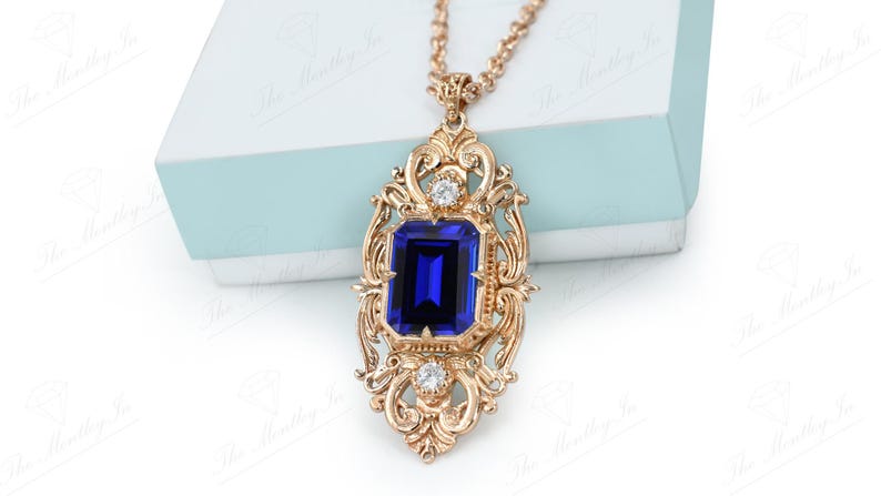 May include: A gold pendant necklace with a large blue gemstone set in a ornate gold frame. The frame is decorated with smaller clear gemstones.