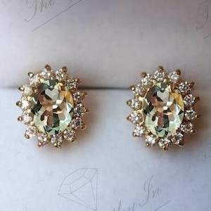 May include: A pair of gold earrings with a large oval green gemstone surrounded by a halo of smaller diamonds.