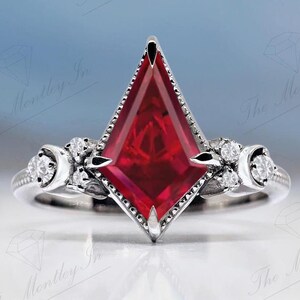 May include: A silver ring featuring a large, red, faceted gemstone in a geometric shape. The ring has smaller, white gemstones set into the band.