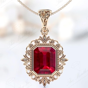 May include: A gold pendant necklace featuring a large, red, emerald-cut gemstone set in a filigree frame.