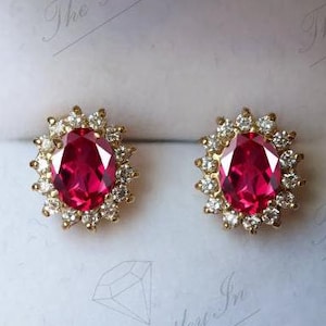 May include: A pair of gold earrings with a large oval-shaped red gemstone surrounded by smaller white gemstones.