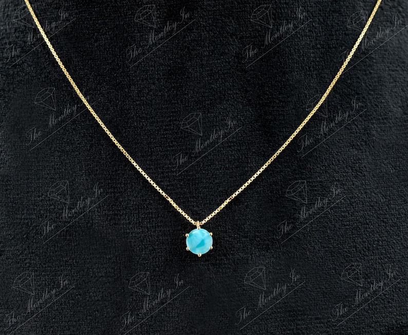 Op de afbeelding: Een gouden ketting met een hanger van turquoise edelsteen. De hanger is een ronde, gefacetteerde steen die in een gouden zetting is gezet.
