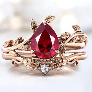 Op de afbeelding: Een ring van roségoud met een peervormige robijn en een kleinere diamant. De ring heeft een delicaat rankontwerp met bladeren.