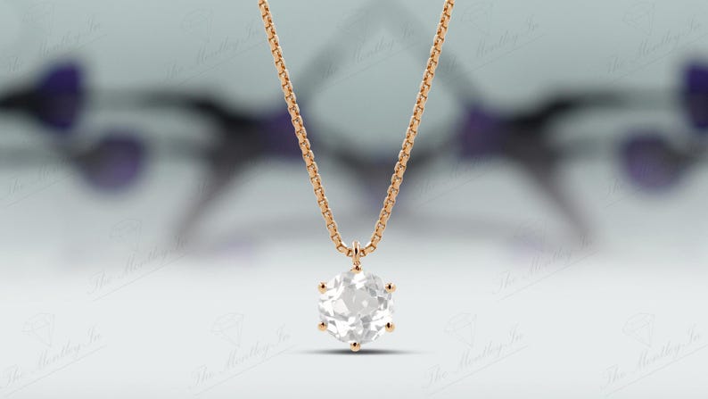 Pu&ograve; includere: Una collana color oro con una catena delicata e un grande pendente di pietra preziosa chiara e sfaccettata. Il pendente &egrave; a taglio brillante, che riflette la luce. Lo sfondo &egrave; sfocato, con sfumature di viola e bianco.