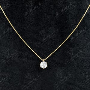 Pu&ograve; includere: Una delicata collana d'oro con un singolo pendente di pietra preziosa trasparente e rotonda. Il pendente &egrave; incastonato in una montatura a sei punte e pende da una sottile catena d'oro. Lo sfondo &egrave; nero.